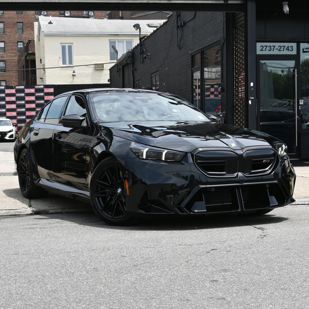 Front three-quarter view of the 2025 BMW M5 Hybrid, showcasing its aggressive stance and Iconic Glow grille.